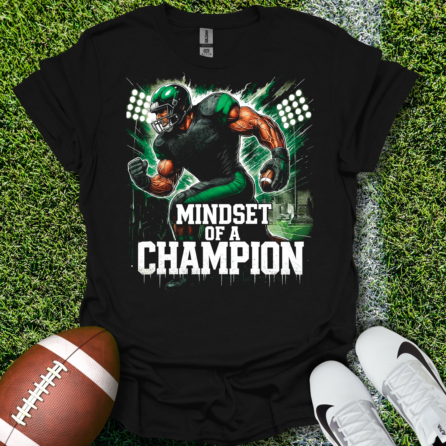 Black t-shirt with a football player graphic and 'Mindset of a Champion' text on grass with a football and shoes.