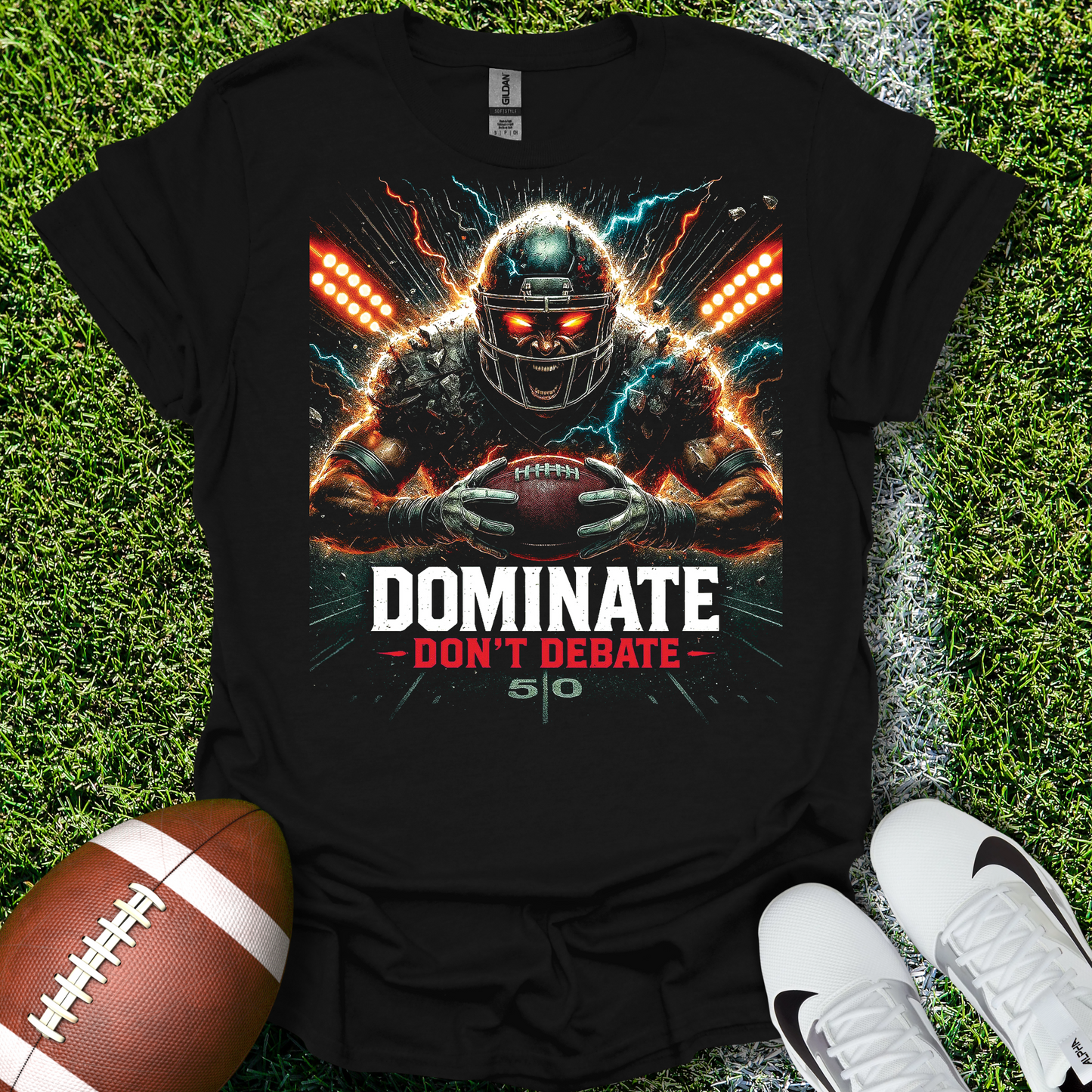 Black t-shirt with football player graphic and text 'DOMINATE DON'T DEBATE' on grass with a football and shoes.