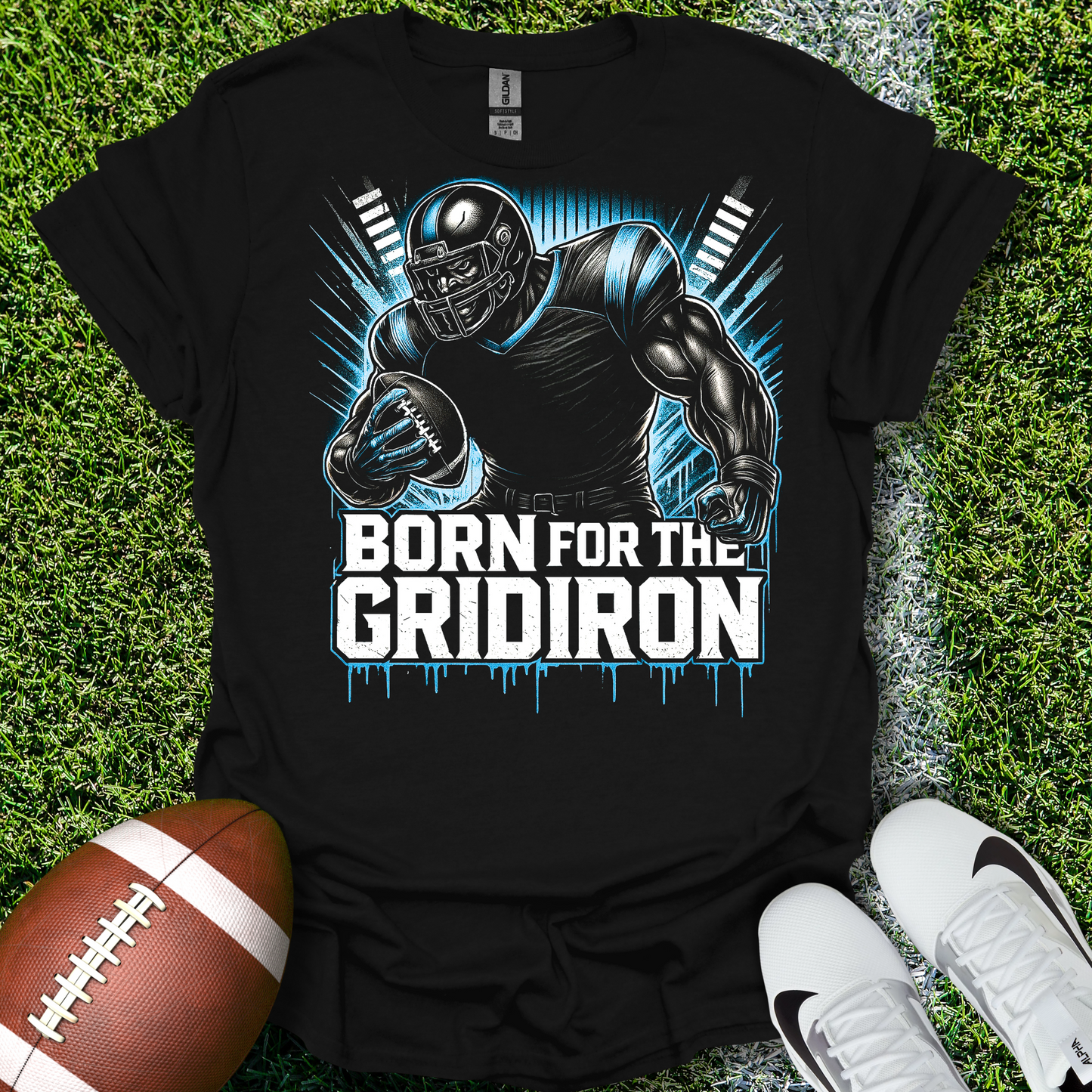 Black t-shirt with football player graphic and 'Born for the Gridiron' text on grass with a football and shoes.
