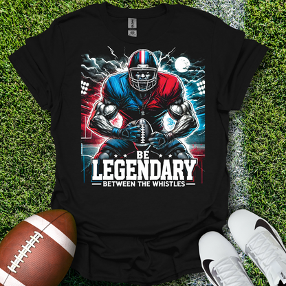 Black t-shirt with football player graphic and 'Be Legendary Between the Whistles' text on grass with a football and shoes.