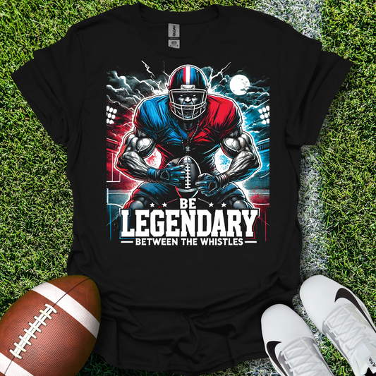 Black t-shirt with football player graphic and 'Be Legendary Between the Whistles' text on grass with a football and shoes.