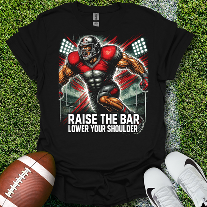 Black t-shirt with a football player graphic and text on grass with a football and shoes.